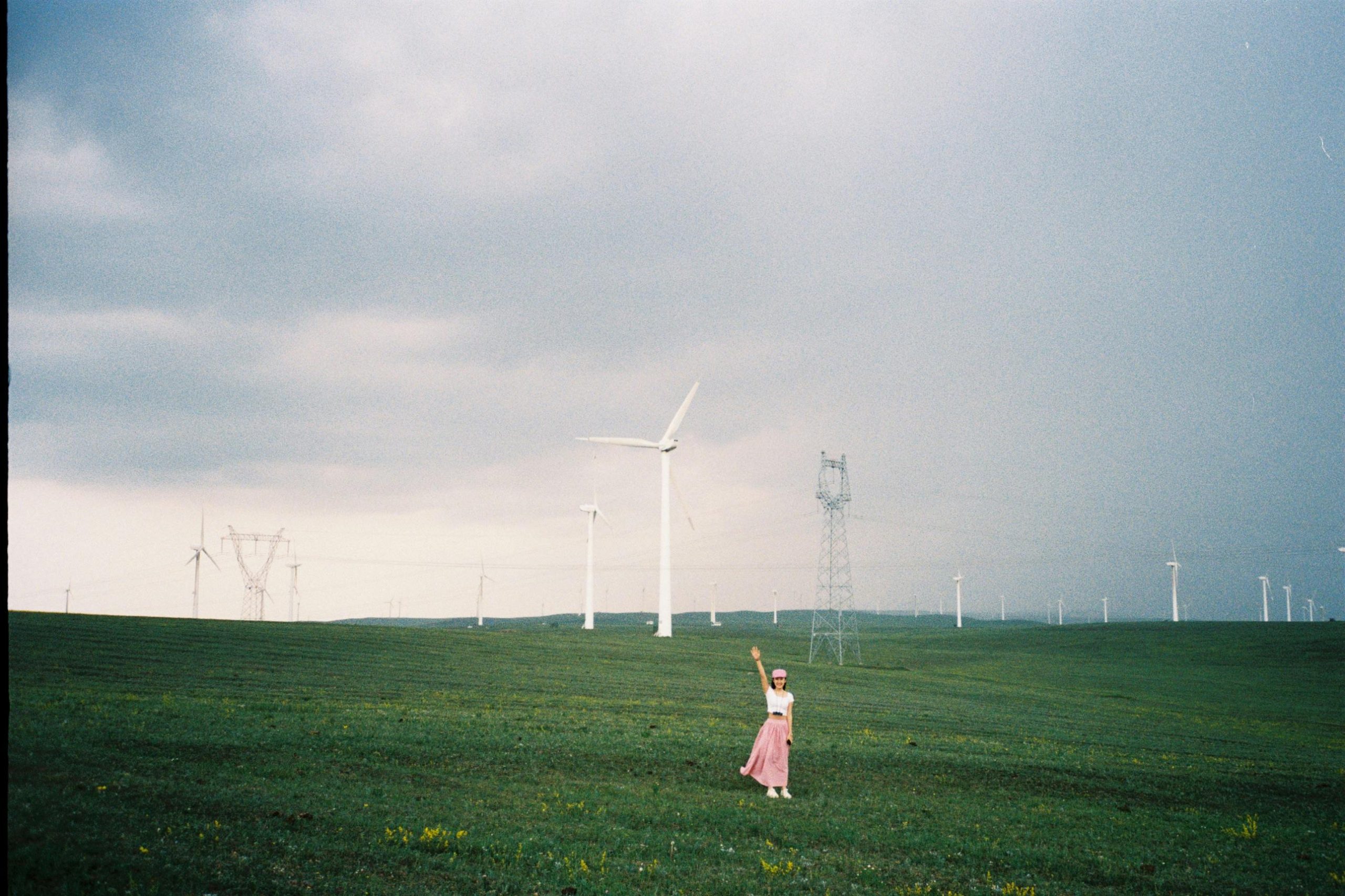 A woman stands在內蒙古的風力發電機田中，遠眺藍天與白雲，感受自由和堅定。